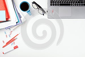 Office table desk with supplies, blank note pad, cup, pen, pc, crumpled paper, flower on white background. Top view