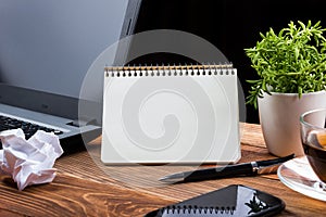 Office table desk with supplies, white blank note pad, cup, pen, pc, crumpled paper, flower on wooden background. Top