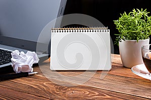 Office table desk with supplies, white blank note pad, cup, pen, pc, crumpled paper, flower on wooden background. Top