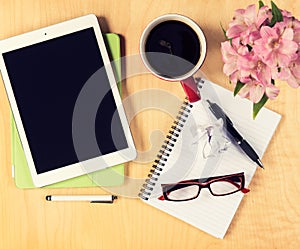 Office table with digital tablet, reading glasses cup of coffee and notepad. View from above