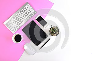 Office table with keyboard, mouse, notebook, digital tablet and smartphone on modern two tone white and pink background