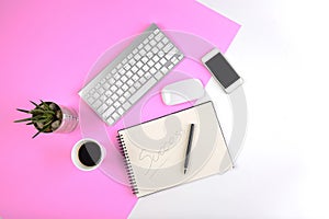 Office table with keyboard, mouse, notebook and smartphone on modern two tone white and pink background