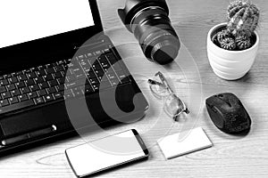 Office table with laptop computer, camera lens, smartphone, eyeglass, mouse and business card.