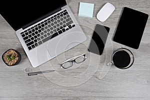 Office table with laptop computer, digital tablet, pen, smartphone, mouse, eyeglasses and coffee on white wood background