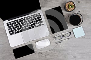 Office table with laptop computer, digital tablet, pen, smartphone, mouse, eyeglasses and coffee on white wood background