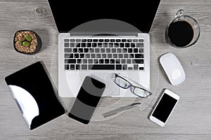 Office table with laptop computer, digital tablet, pen, smartphone, mouse, eyeglasses and coffee on white wood background