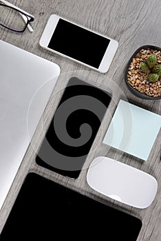 Office table with laptop computer, digital tablet, pen, smartphone, mouse, eyeglasses and coffee on white wood background