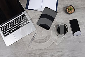 Office table with laptop computer, notebook, digital tablet, pen, smartphone, mouse and coffee on white wood background