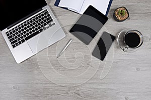 Office table with laptop computer, notebook, digital tablet, pen, smartphone, mouse and coffee on white wood background