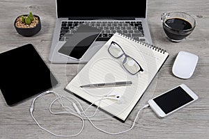 Office table with laptop computer, notebook, digital tablet, pen, smartphone, mouse, eyeglasses and coffee on wood background