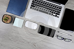 Office table with laptop computer, notebook, digital tablet, pen, smartphone, mouse, eyeglasses and coffee on wood background