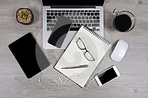 Office table with laptop computer, notebook, digital tablet, pen, smartphone, mouse, eyeglasses and coffee on wood background