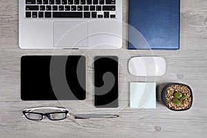 Office table with laptop computer, notebook, digital tablet, pen, smartphone, mouse, eyeglasses and coffee on wood background