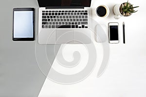 Office table with laptop computer, notebook, digital tablet and smartphone on modern two tone white and grey background