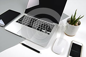 Office table with laptop computer, notebook, digital tablet and smartphone on modern two tone white and grey background