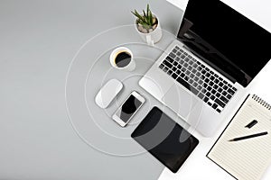 Office table with laptop computer, notebook, digital tablet and smartphone on modern two tone white and grey background