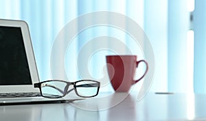 Office table with notebook laptop, eading glasses and coffee mug. Copy space