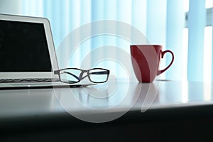 Office table with notebook laptop, eading glasses and coffee mug. Copy space