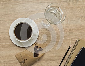 Office table with notepad, smart phone, coffee cup, glass of water and dark chocolate. Top view of work place