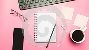 Office table in pastel pink colors with laptop, smartphone, keyboard, coffee cup and notebook. Top view, copy space, flat lay