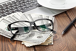 Office table with pc, coffee cup and glasses over money cash