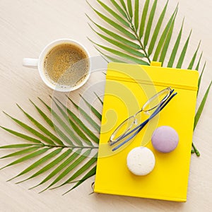 office table with yellow notepad, cup of coffee, glasses, macaroons on palm