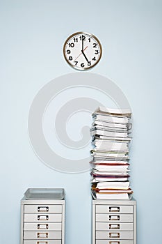 Office wall with clock stack of paperwork in outbox on file cabinet photo