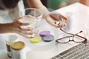 Office women pouring the pills vitamin,supplements out of the bottle on hand and holding a glass of water at home office.