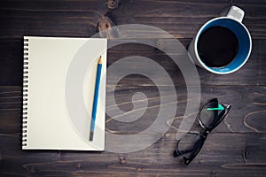 Office wood table with blank notepad, pencil, glasses and cup of