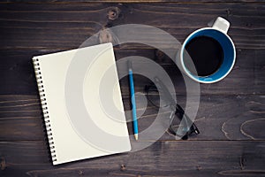 Office wood table with blank notepad, pencil, glasses and cup of