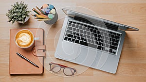 Office wooden desk workplace with laptop computer, notebook, pen, eyeglass and cup of coffee, Top view