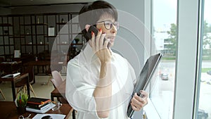 Office work concept. A mature businesswoman stands by the window and talks on the phone