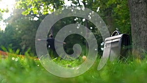 Office worker dancing on background, briefcase standing on grass, happiness