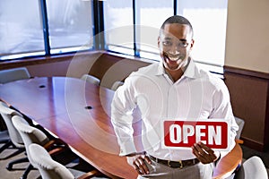 Office worker holding open sign in empty boardroom