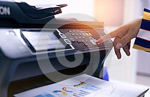 Office worker print paper on multifunction laser printer. Copy, print, scan, and fax machine in office. Modern print technology.