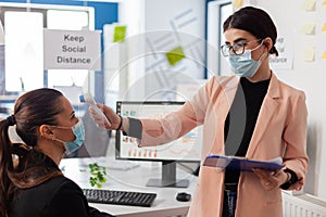 Office worker scanning colleague temperature pointing digital thermometer