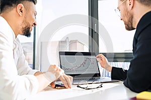 Office worker showing company income chart on laptop to his boss.