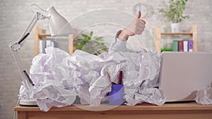 Office worker shows a thumbs up from a large heaps of papers