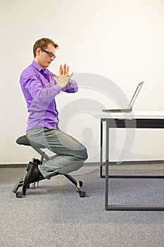 Office worker sitting on kneeling stool, exercising during short break in work