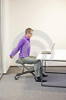 Office worker sitting on kneeling stool, stretching arms