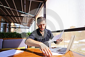 Office worker sorting papers on table near laptop.