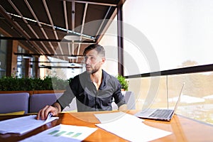 Office worker sorting papers on table near laptop.