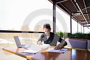 Office worker sorting papers on table near laptop.