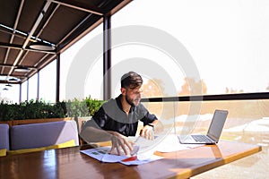 Office worker sorting papers on table near laptop.