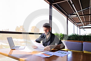 Office worker sorting papers on table near laptop.