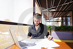 Office worker sorting papers on table near laptop.