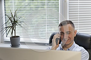 Office worker speaks on phone while sitting at his workplace. Young boss is speaking on phone