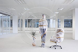 Office worker swivel chair and potted plant covered with bubble wrap and tape in empty office space photo
