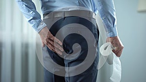 Office worker with toilet paper in hand suffering from hemorrhoid pain, diarrhea