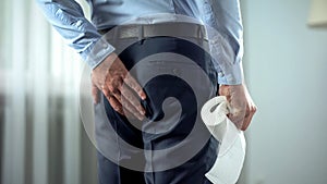 Office worker with toilet paper in hand suffering from hemorrhoid pain, diarrhea